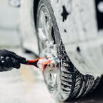 Carwash service, car in foam, side view. Auto detailing, washing of wheels with brush