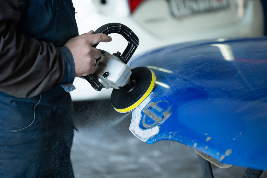 A man who sanding with a grinder and prepares the paint for the car in a car service. Repairman fix car paint.