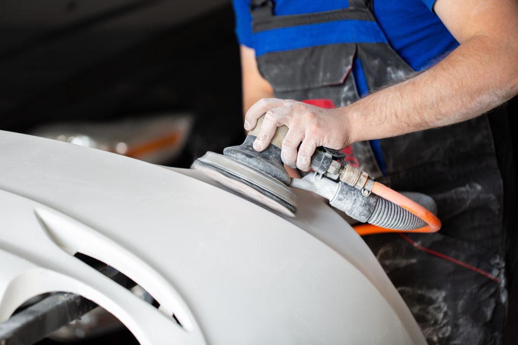 A man who sanding with a grinder and prepares the paint for the car in a car service. Repairman fix car paint.