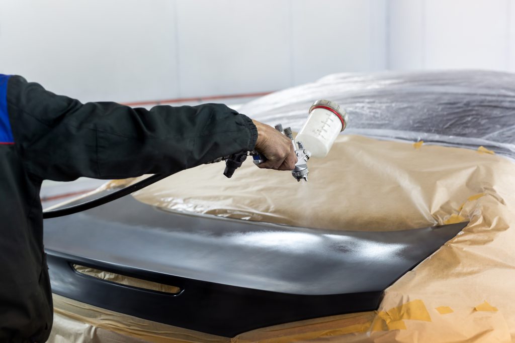Close-up of a spray gun with black paint for painting a car in a special booth.