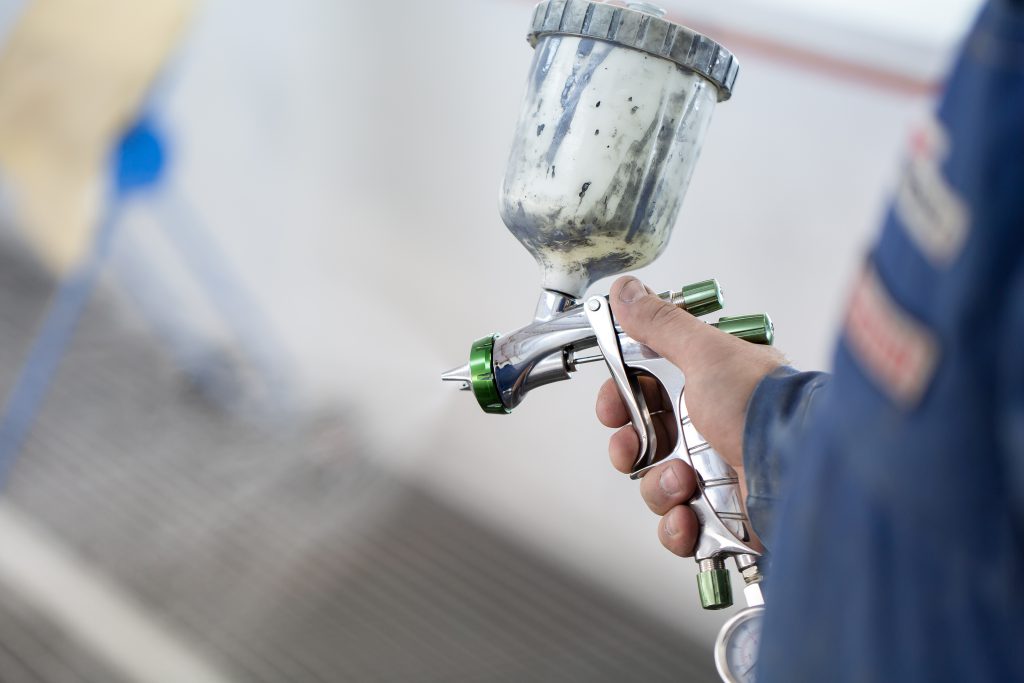 Close-up of a spray gun with white paint for painting a car in a special booth.