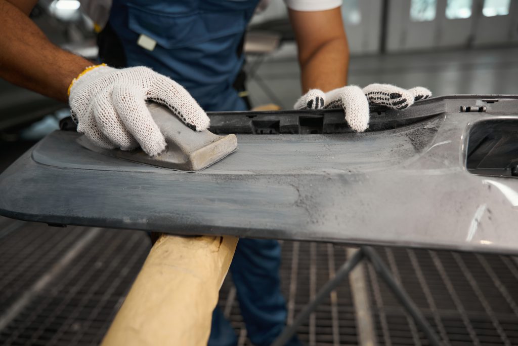 Mechanic in protective gloves holding grinding tool and cleaning surface before priming in tire fitting