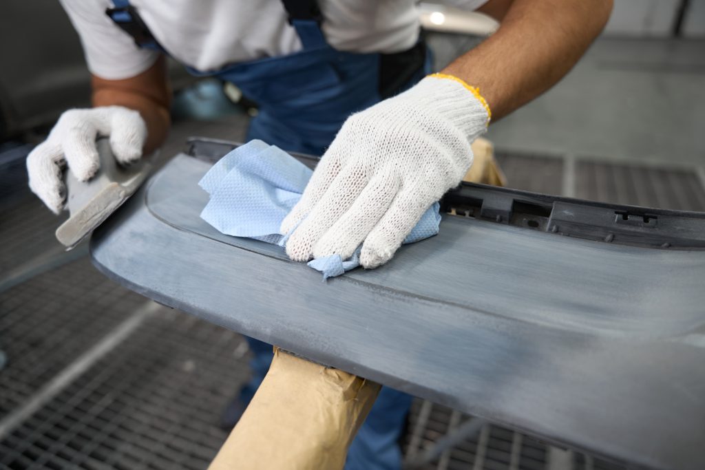 Fitter in protective gloves and special suit holding grinding tool and cleaning surface before priming in tire fitting