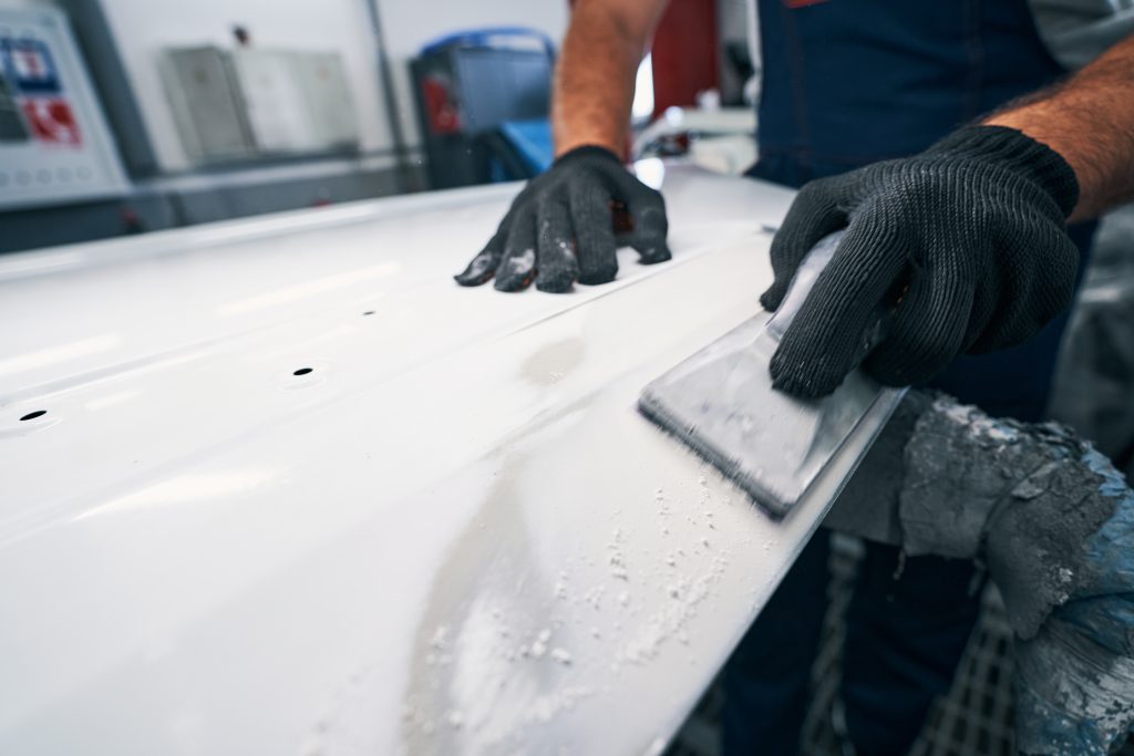 Man using hand sander for peeling off paint layer from automobile external surface in repair shop